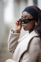 An elegant young woman peers over her sunglasses, exuding confidence and style. Her headband...