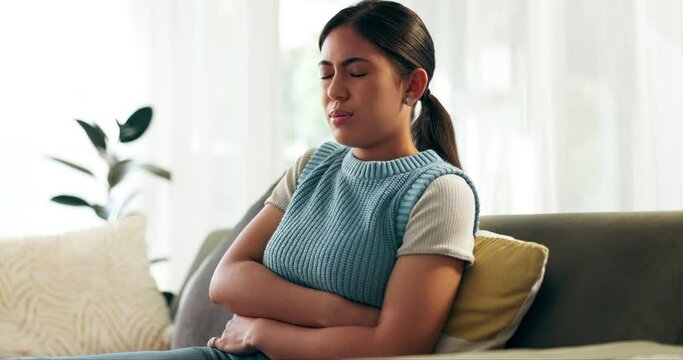 Anxiety, stomach pain and Asian woman on sofa in living room with menstruation, gas or constipation at home. Gut health, sick and person with tummy ache for pms, nausea or endometriosis at apartment.