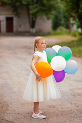 A beautiful elegant girl in a fluffy white dress holds bright colorful balloons in her hands.