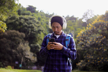 Young Asian man in a casual outfit, sporting a beanie, plaid shirt, and headphones, checks his...
