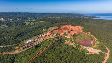 aerial landscape view around a Bauxite mining plant located within a green forest with ocean in the background and orange surface around the mine