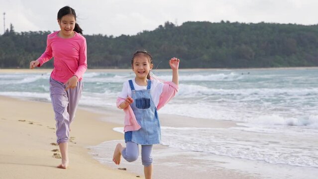 slow motion of two happy asian kids running on the beach at Riyue Bay Wanning Hainan China, kids fun holiday with ocean