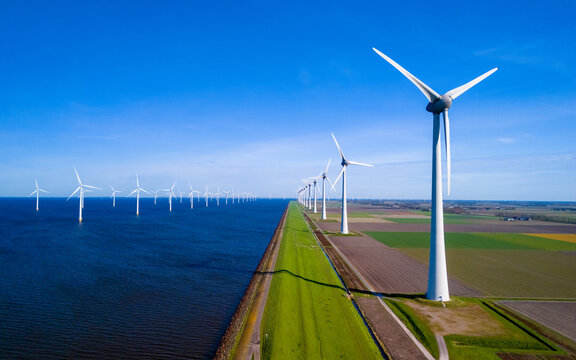A striking line of wind turbines gracefully spinning next to a vast body of water in theNetherlands