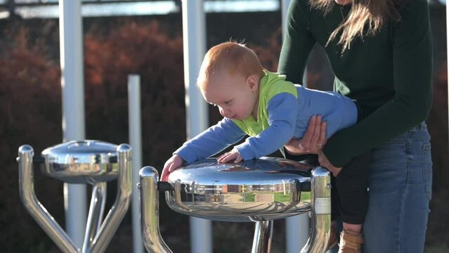 One year old gold hair bboy with mother In the park,play the outdoor musical instrument Babel Drums, laughing happily.