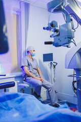 An oculist doctor sits on the background of a modern microscope for vision testing in the office. Medical room for vision treatment