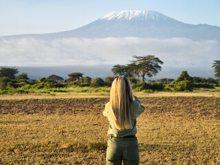 young beautiful blonde walks through the savannah against the backdrop of Mount Kilimanjaro during...