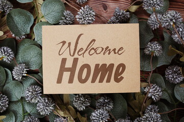 Welcome Home text message on paper card with flowers border frame on wooden background