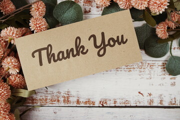 Thank You text message on paper card with flowers border frame on wooden background