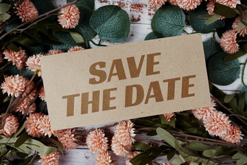 Save the Date text message on paper card with flowers border frame on wooden background