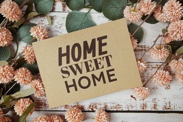 Home Sweet Home text message on paper card with flowers border frame on wooden background