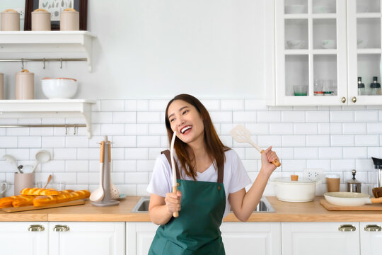 Young Asian woman dancing in the kitchen. The joy of a beautiful woman relaxing in her free time during the weekend in the house