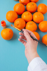 Female hand holding brush and paint on orange. Vibrant vertical photo of many citrus fruits top...