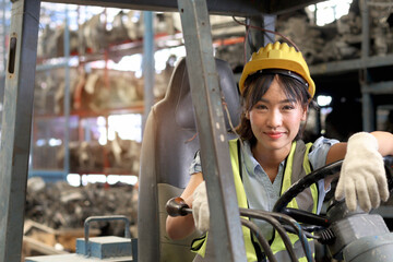 Industrial worker woman wearing safety vest and helmet driving forklift car at manufacturing plant...