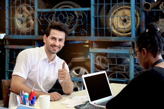 Happy man is pleased, give thumb up with suggestions, products and services. Buyer talks with staff at counter in auto spare parts store with secondhand engine. Customer appreciate provided deals.