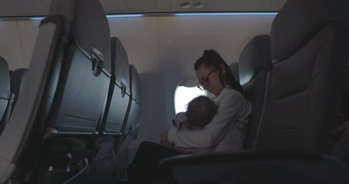 Mother holding infant daughter while flying on airplane - side profile in empty airplane