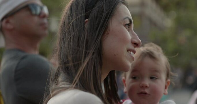 Mother holding toddler watching parade event outdoors - close up on face