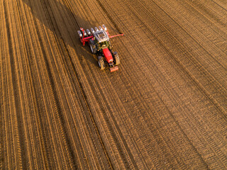 Aerial shot of a farmer seeding, sowing crops at field. Sowing is the process of planting seeds in the ground as part of the early spring time agricultural activities. - obrazy, fototapety, plakaty