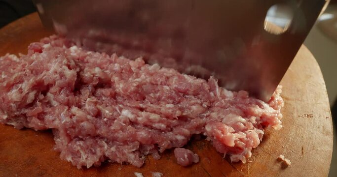 Pork mincing on a wooden chopping block with a cleaver
