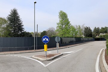 Double arrow traffic sign, or split road sign, at the end of a roundabout. Black antinoise panels...