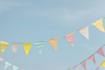 A bunch of colorful pastel colors flags hanging in the sky, with a blue sky in the background, party and birthday background. - Powered by Adobe