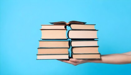 A hand holds a stack of books against a blue background. 