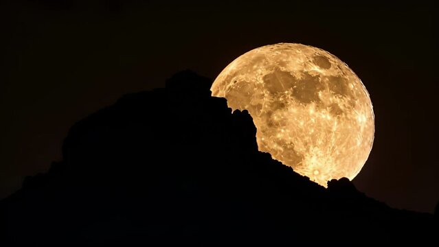 A majestic supermoon rising over the silhouette of a solitary mountain peak. . .