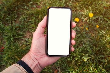 Smartphone mockup, male hand holding mobile phone with blank white screen in park on spring morning - 780311633