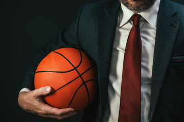 Basketball coach in elegant business suit holding the ball on dark background
