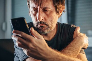 Man reading text message on mobile phone, unkempt male holding cell phone indoors