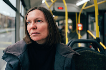 Contemplative adult caucasian woman riding public transportation bus through city streets - 780311864