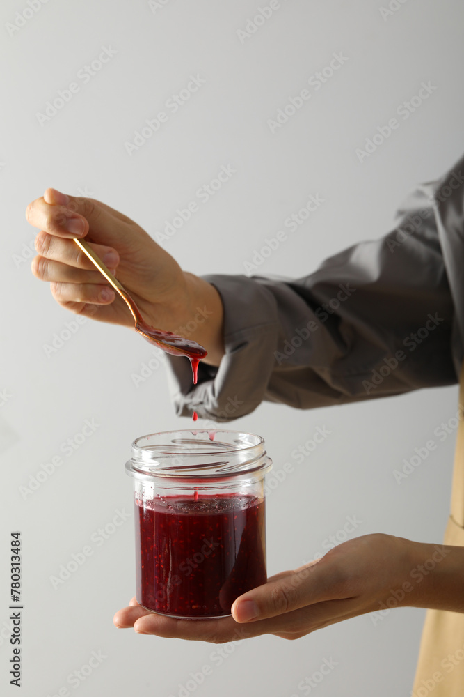 Sticker glass jar with fig jam and spoon in female hands on white background