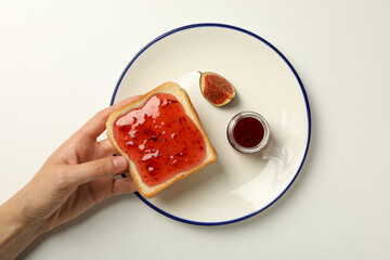 Fig jam, plate and toaster bread in hand on white background, top view