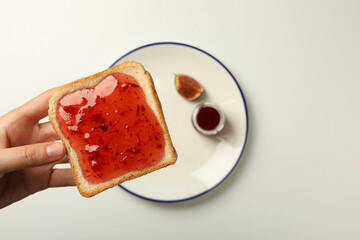 Fig jam, plate and toaster bread in hand on white background, top view