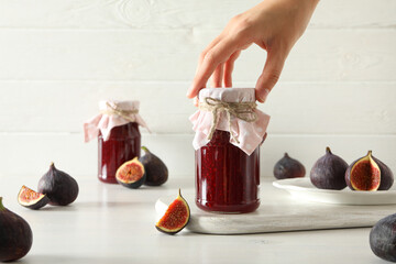 Jars with fig jam, whole and cut figs, female hand on light background
