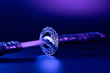 Close-up of samurai sword replica with a decorative hilt, illuminated by a neon light. Intricate...