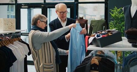 Senior couple shopping for formal outerwear at fashion boutique, looking for trendy elegant...