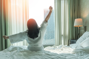 Hotel relaxation on lazy day with Asian woman waking up from good sleep on bed in weekend morning resting in comfort bedroom looking toward city view, having happy, work-life quality balance lifestyle - 780323607