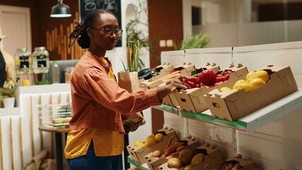 African american buyer choosing organic produce from crates, putting fruits and veggies in a paper bag to purchase. Woman shopping for natural eco friendly products at local farmers market. Camera 1.
