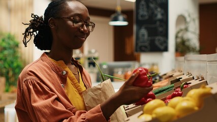 Vegan woman taking locally grown vegetables from crates, going grocery shopping at local farmers market. Regular customer choosing colorful ripe produce, nonpolluting farming business. Camera 1. - obrazy, fototapety, plakaty