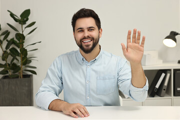 Happy young man waving hello during video chat indoors, view from web camera