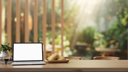 A laptop computer with a white screen mockup on a rustic wooden table in a beautiful cafe garden.