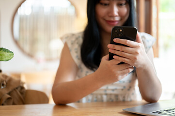 A cropped image of a happy Asian woman using her smartphone while sitting in a cafe.