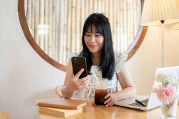 A happy, charming young Asian woman relaxing in a coffee shop and using her smartphone.