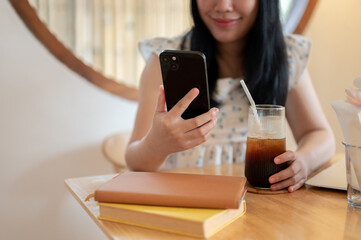 A cropped image of an Asian woman relaxing in a coffee shop and using her smartphone.