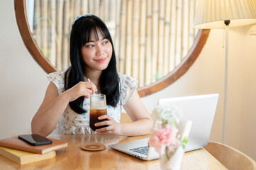 A beautiful Asian woman enjoys her iced coffee and daydreaming in a minimalist coffee shop.