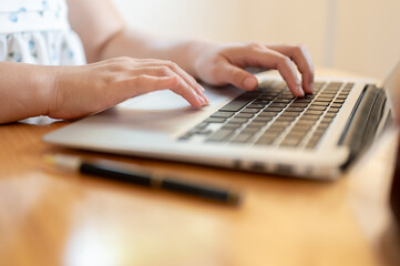 A close-up image of a woman using her laptop at a table indoors, typing on the laptop keyboard.