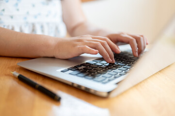 A close-up image of a woman using her laptop at a table indoors, typing on the laptop keyboard.