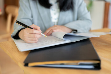 A cropped image of a businesswoman reading and signing on a document at a table.