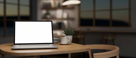 A laptop computer mockup on a wooden table in a minimalist comfortable coffee shop at night