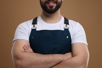 Smiling man in kitchen apron with crossed arms on brown background, closeup. Mockup for design